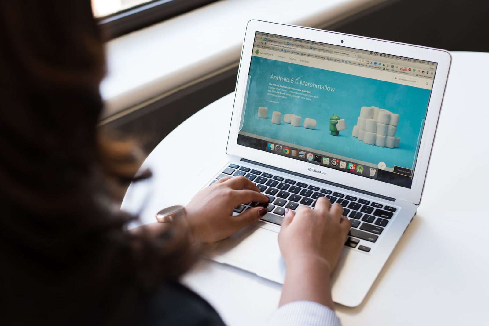 Frau tippt auf einem MacBook Air auf einem weißen Tisch, auf dem Bildschirm ist ein Browser geöffnet