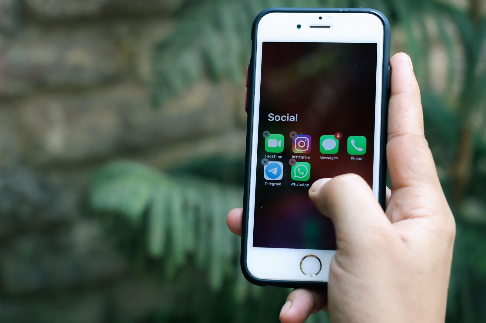Main tenant un smartphone affichant un dossier « Social » avec des applications de messagerie et d'appel vidéo
