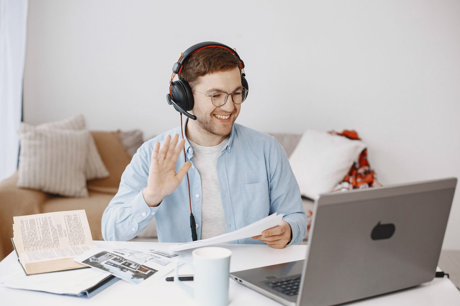 Homme souriant avec casque audio saluant de la main devant un ordinateur portable lors d'un appel vidéo