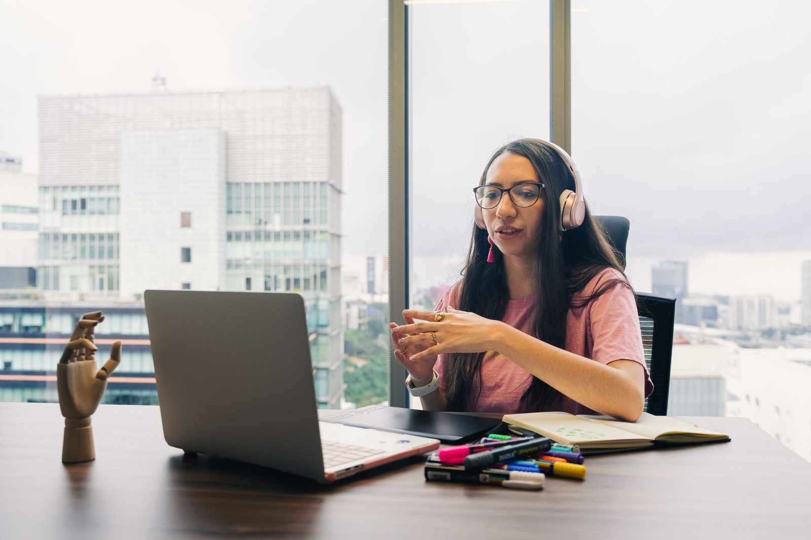 Jeune femme avec casque audio et lunettes en visioconférence devant un ordinateur portable, dans un bureau