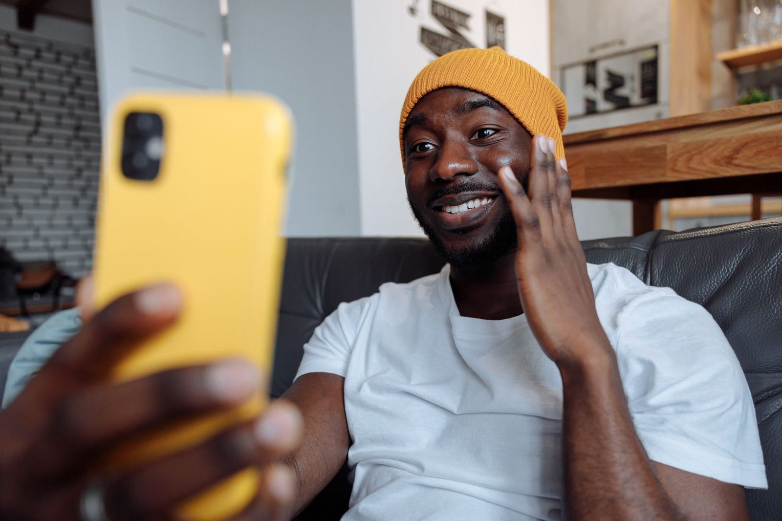 Homme souriant au bonnet jaune faisant un signe de la main lors d'un appel vidéo sur son smartphone