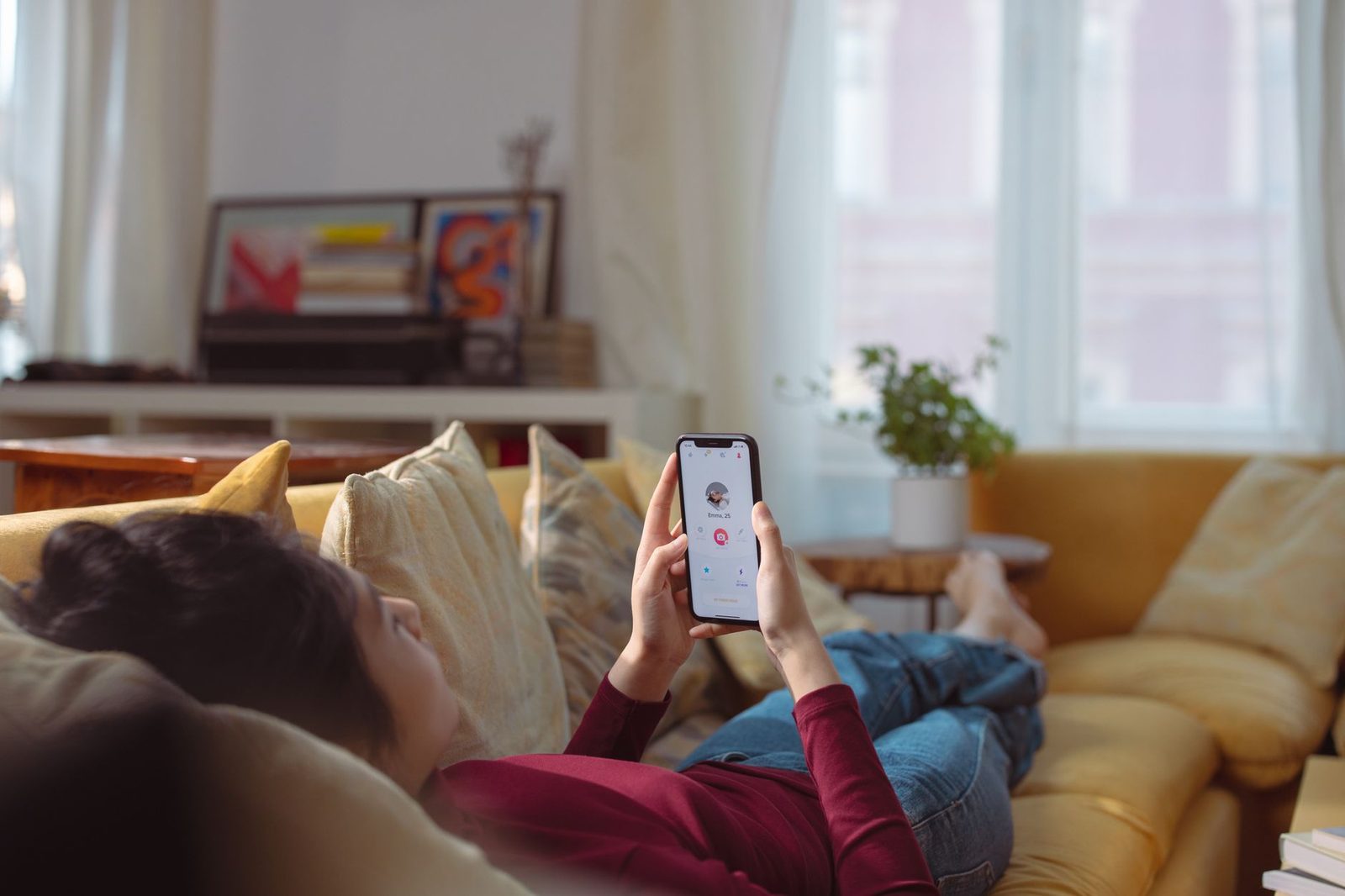 Jeune femme allongée sur un canapé jaune utilisant une application de rencontre sur son smartphone