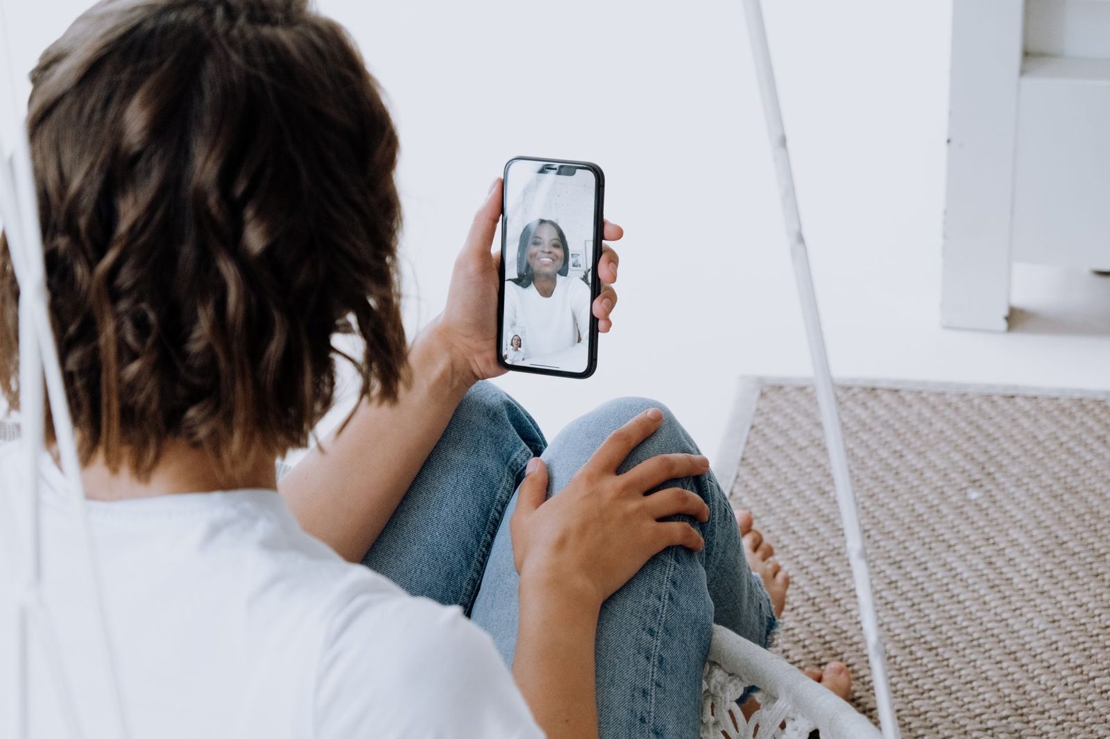 Femme assise tenant un smartphone pendant un appel vidéo avec une autre femme souriante à l'écran