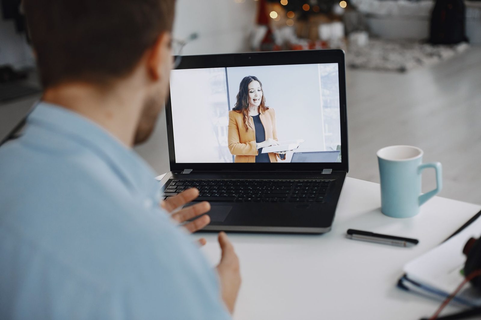 Man op de rug gezien achter een laptop tijdens een videogesprek met een vrouw op het scherm, mok op het bureau
