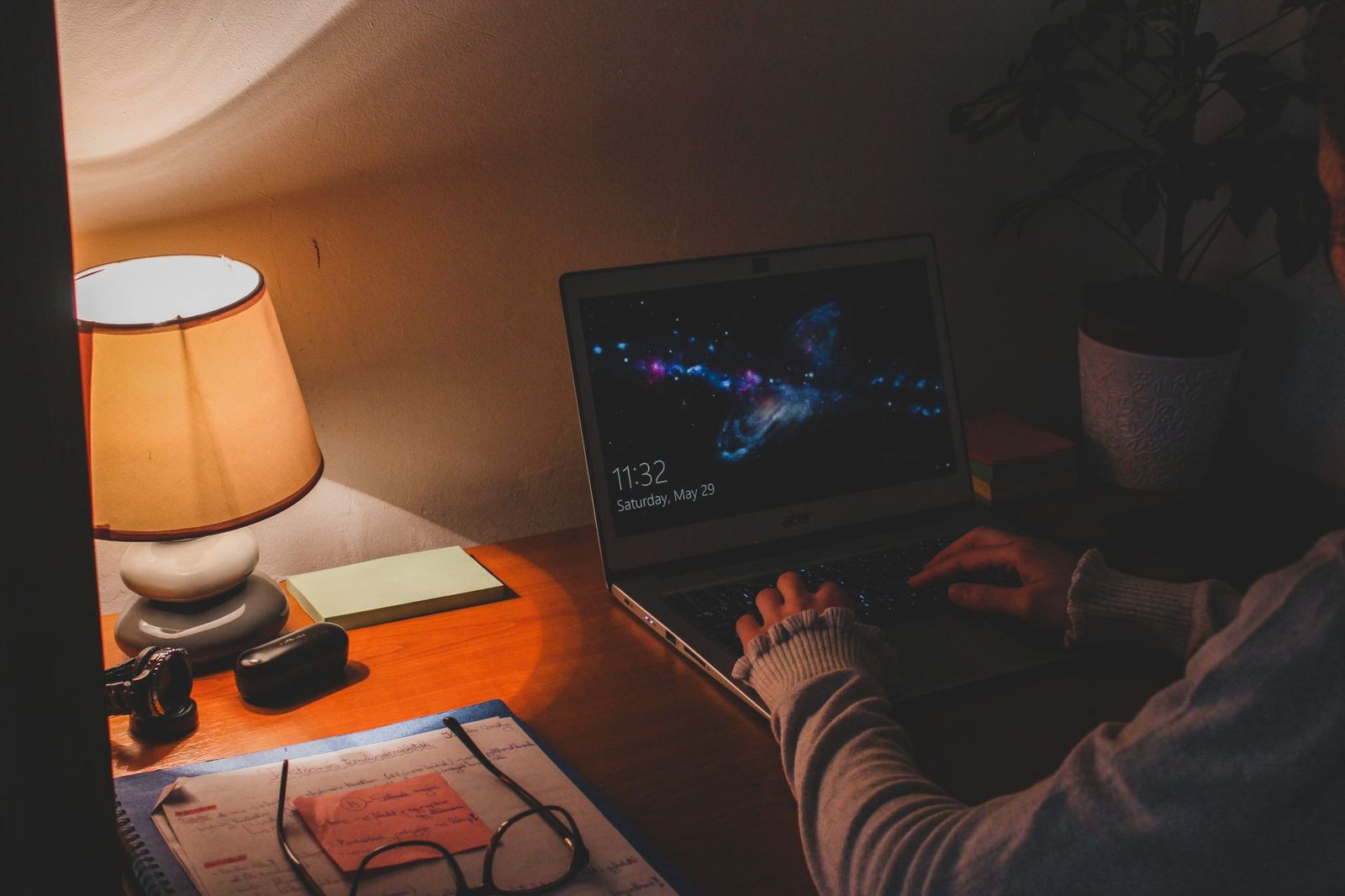 Personne tapant sur un ordinateur portable à webcam, le soir, à un bureau éclairé par une lampe