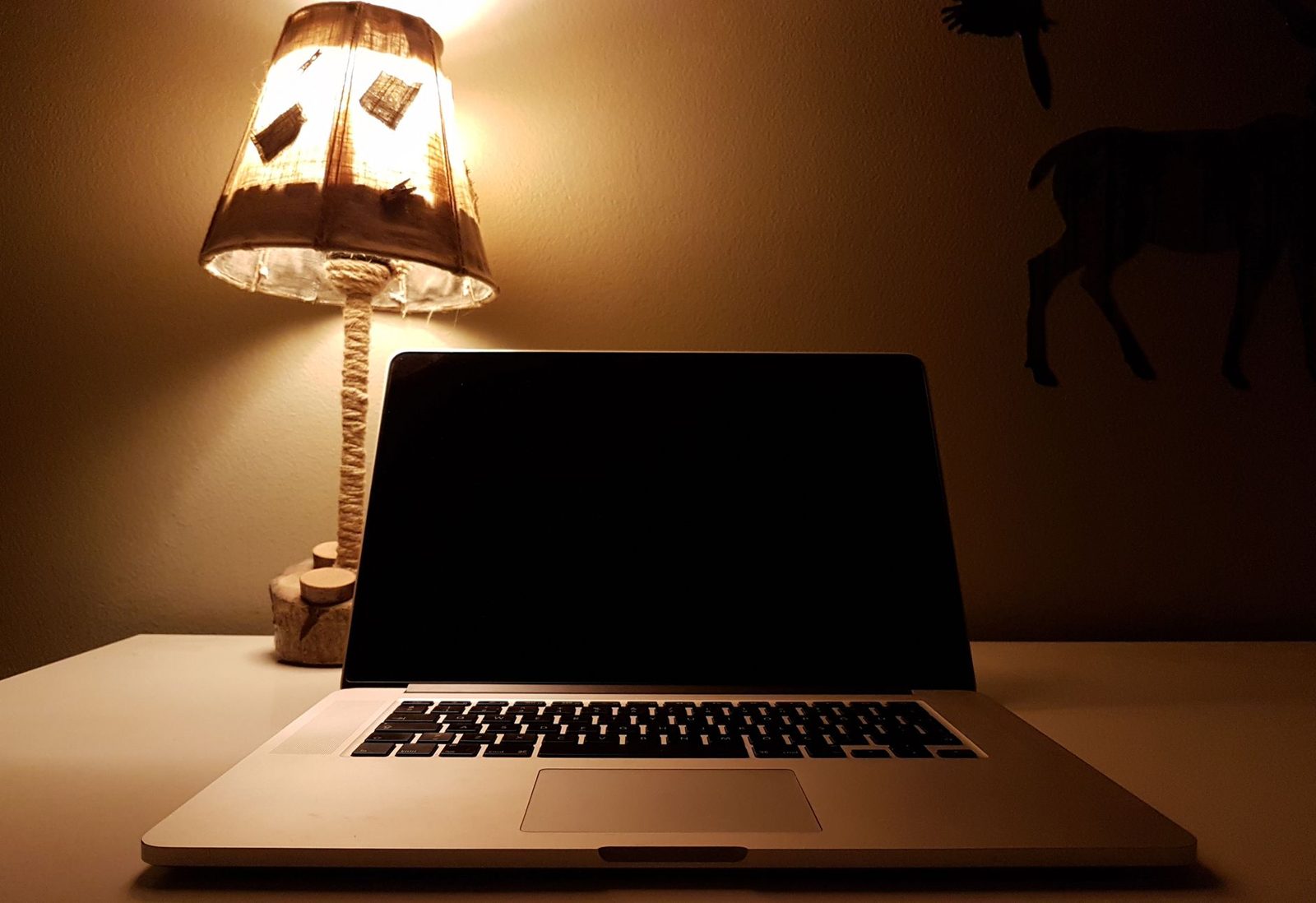 Ordinateur portable ouvert à l'écran éteint sur un bureau, éclairé par une lampe de chevet dans une pièce sombre
