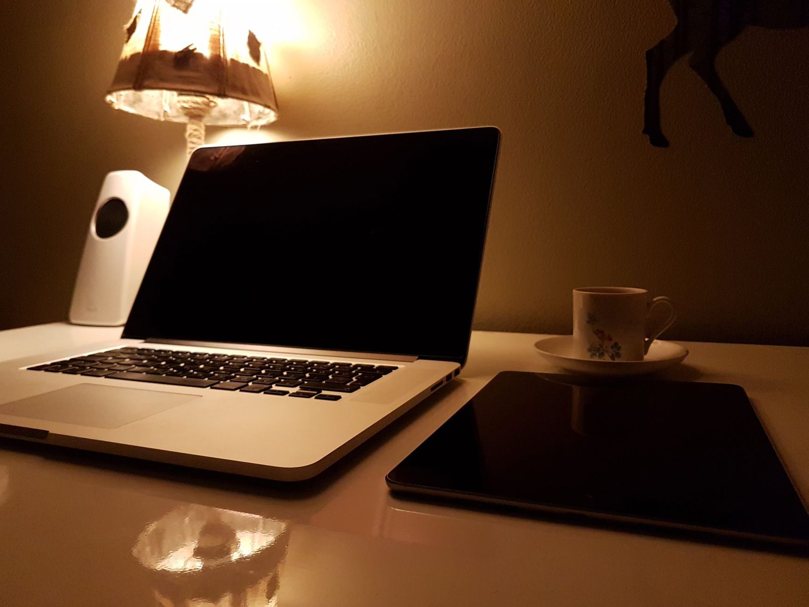 Ordinateur portable ouvert, tablette et tasse de café sur un bureau blanc éclairé par une lampe