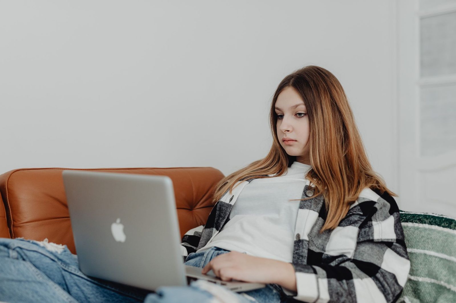 Ragazza seduta su un divano, che guarda lo schermo di un computer portatile appoggiato sulle gambe