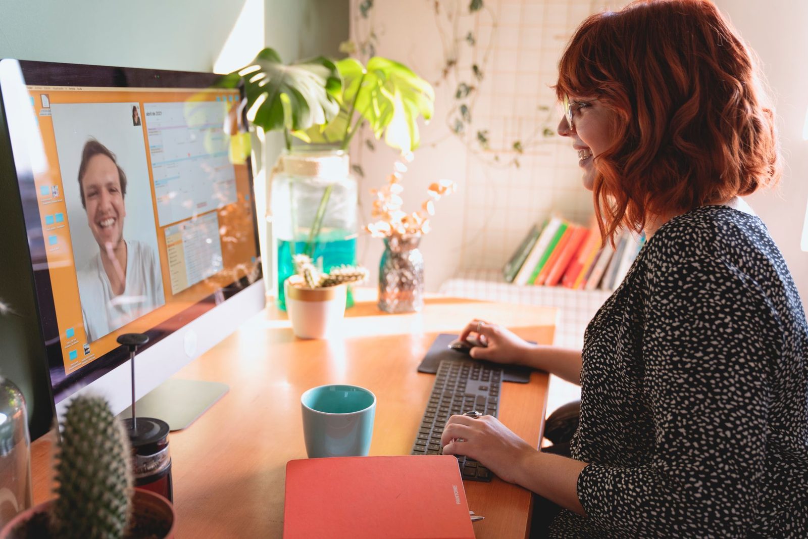 Smiling woman on a video call with a man displayed on her computer screen, at her desk