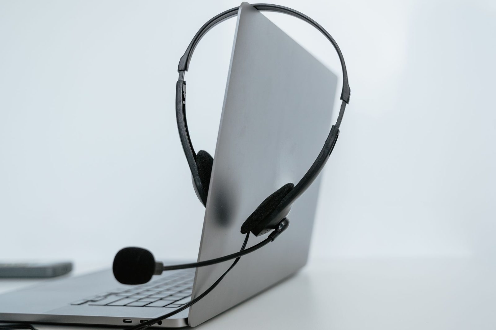 Black headset microphone resting on a half-open grey laptop against a white background