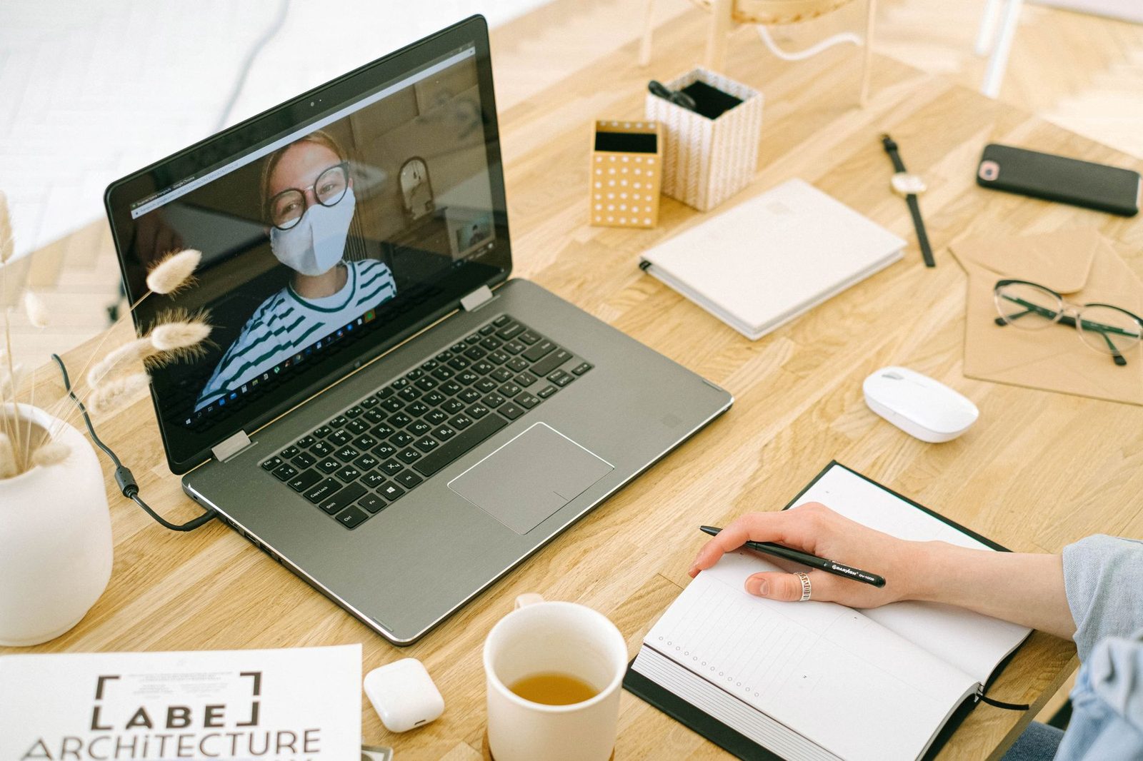 Appel vidéo sur un ordinateur portable posé sur un bureau en bois, avec carnet, stylo et tasse de thé