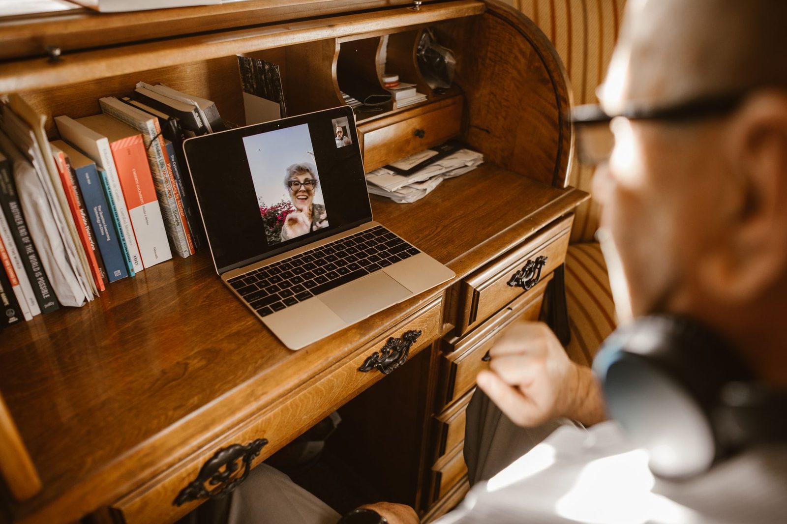 Homme âgé avec casque audio en appel vidéo sur un ordinateur portable posé sur un bureau en bois