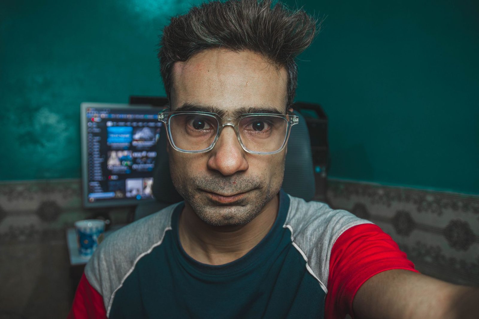 Homem de óculos a tirar uma selfie diante de um ecrã de computador com uma janela de conversa em vídeo
