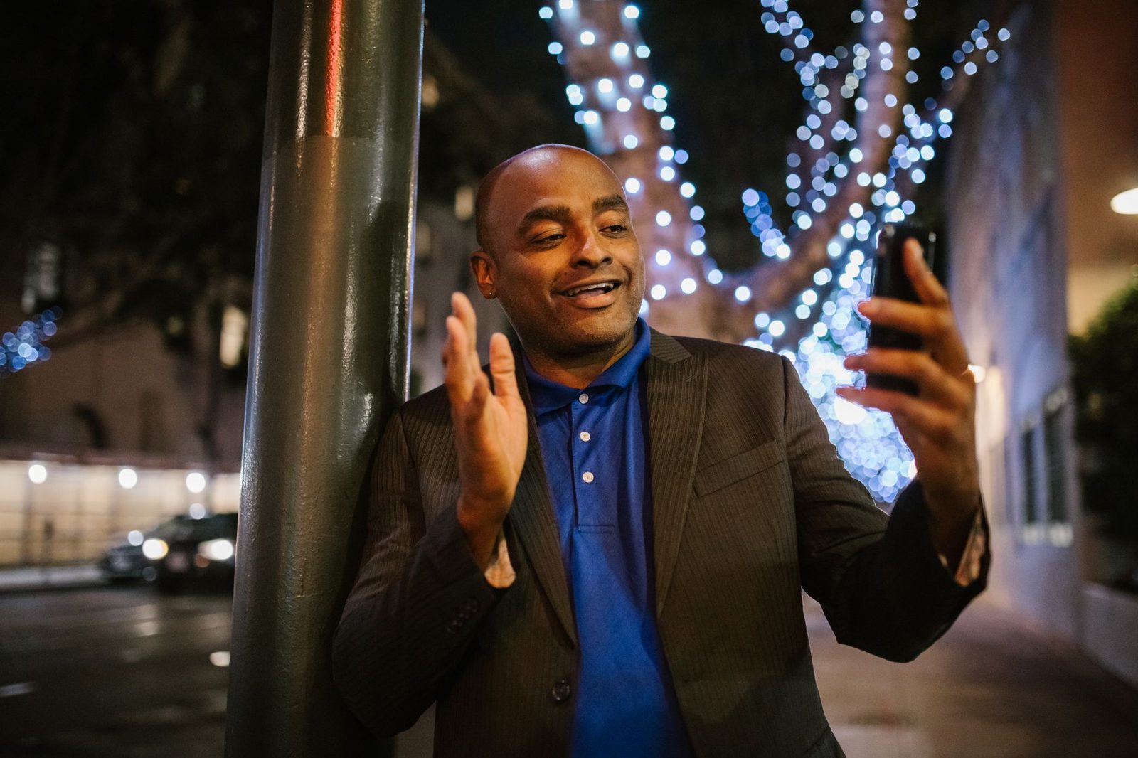 Homme souriant en veste passant un appel vidéo sur son smartphone dans une rue illuminée la nuit