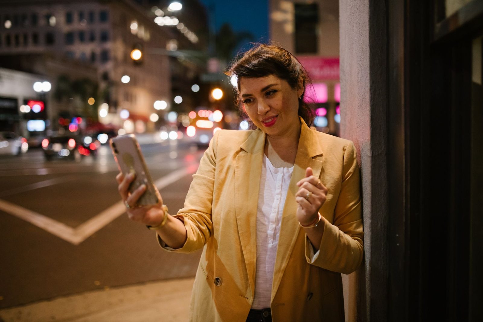Femme en veste jaune passant un appel vidéo sur son smartphone dans une rue de ville la nuit