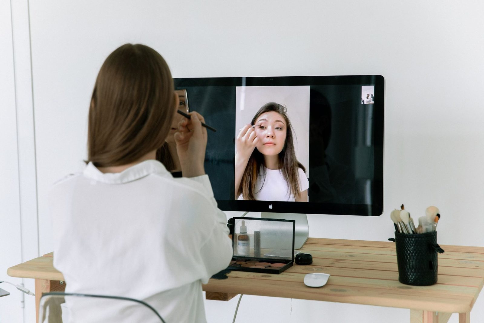 Femme de dos devant un écran d'ordinateur affichant une autre femme en appel vidéo