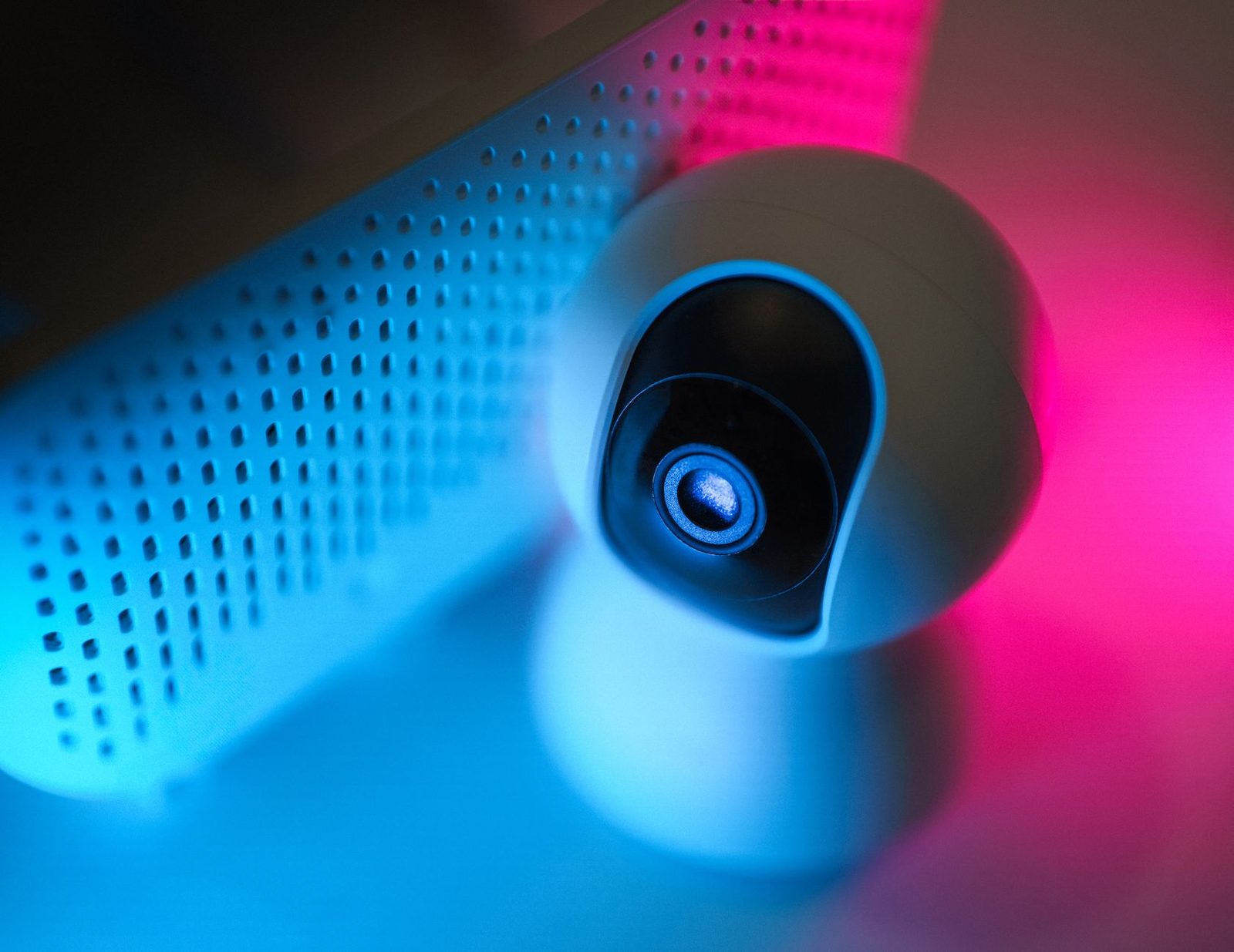 Webcam blanche en gros plan posée près d'une enceinte, éclairée de lumières bleue et rose