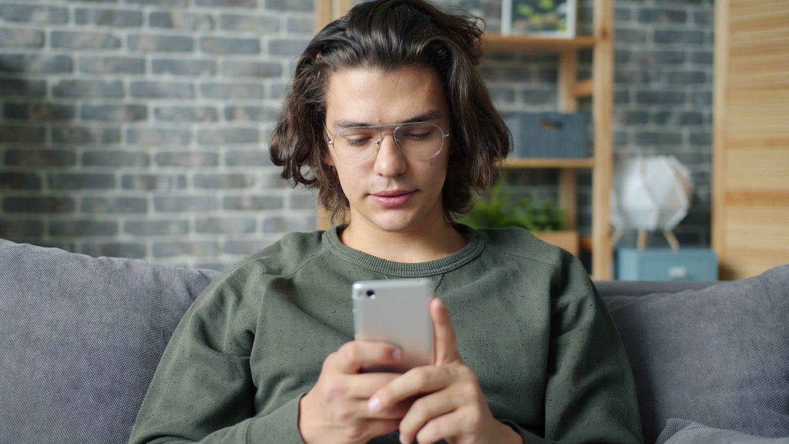 Jovem de óculos sentado num sofá, a usar o smartphone numa sala de estar