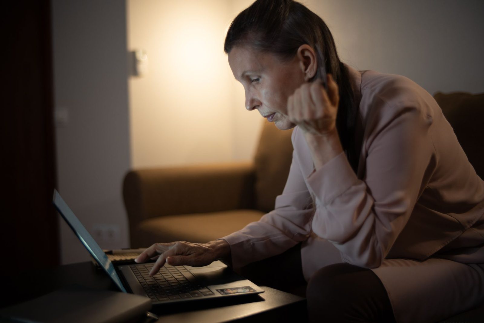 Femme assise sur un canapé utilisant un ordinateur portable le soir dans une pièce faiblement éclairée