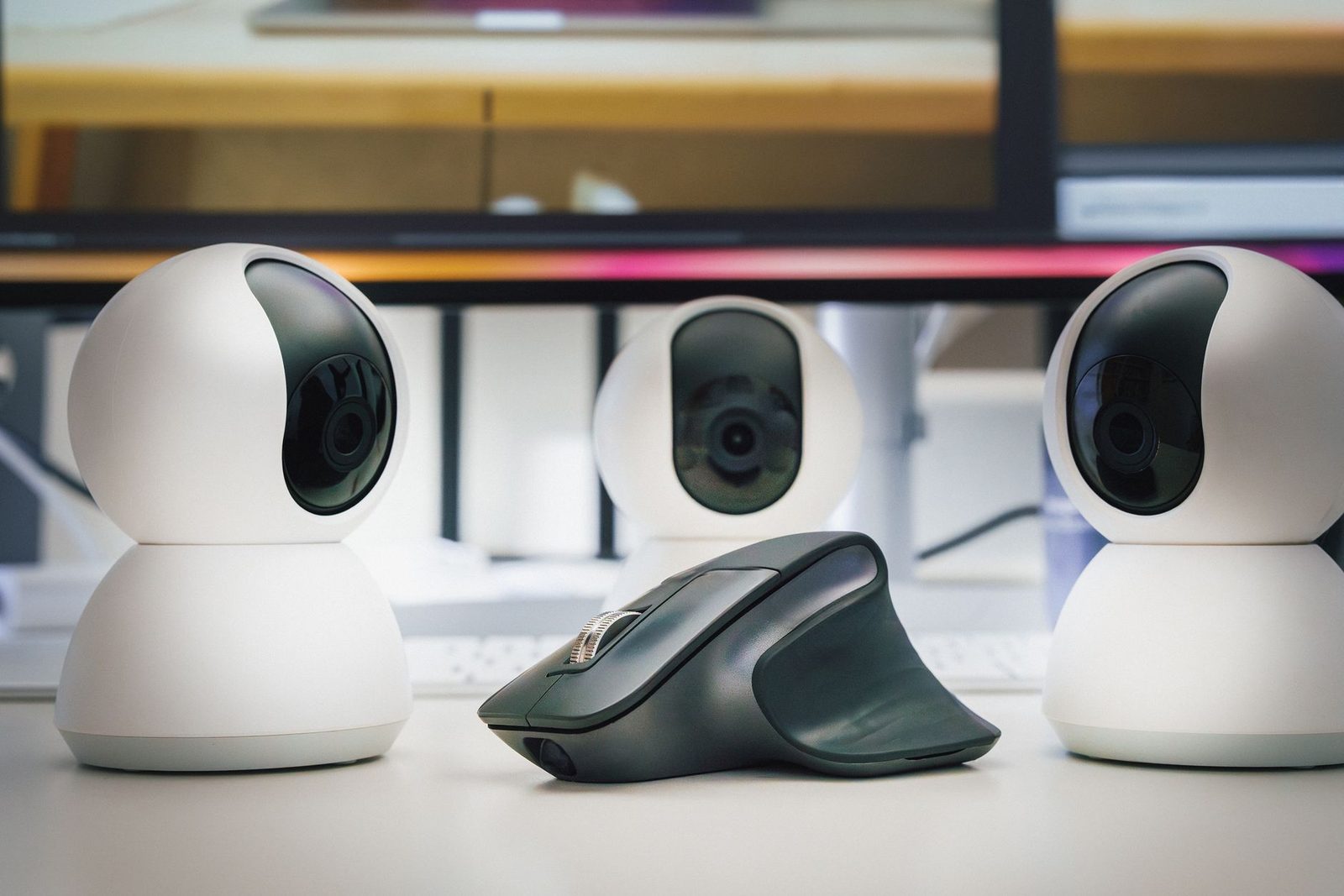 Trois webcams blanches et une souris sans fil posées sur un bureau devant un écran d'ordinateur