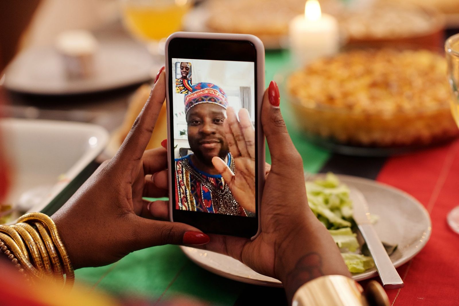 Mains tenant un smartphone affichant un appel vidéo avec un homme, devant une table de repas