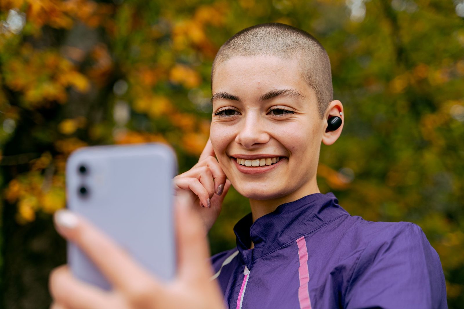 Jeune femme souriante avec écouteurs sans fil regardant l'écran de son smartphone en extérieur