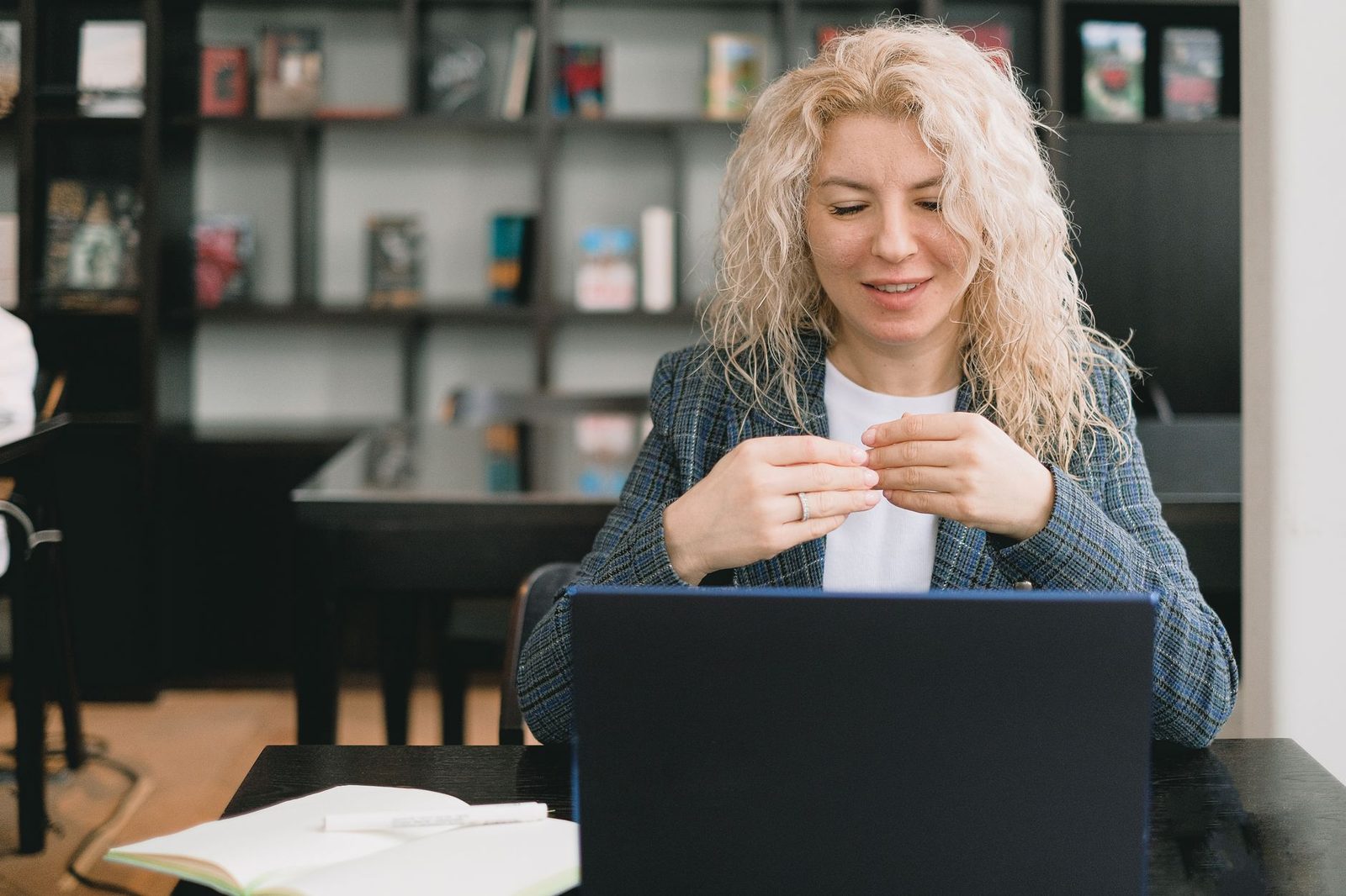 Jeune femme blonde souriante devant un ordinateur portable, en pleine conversation vidéo dans une bibliothèque