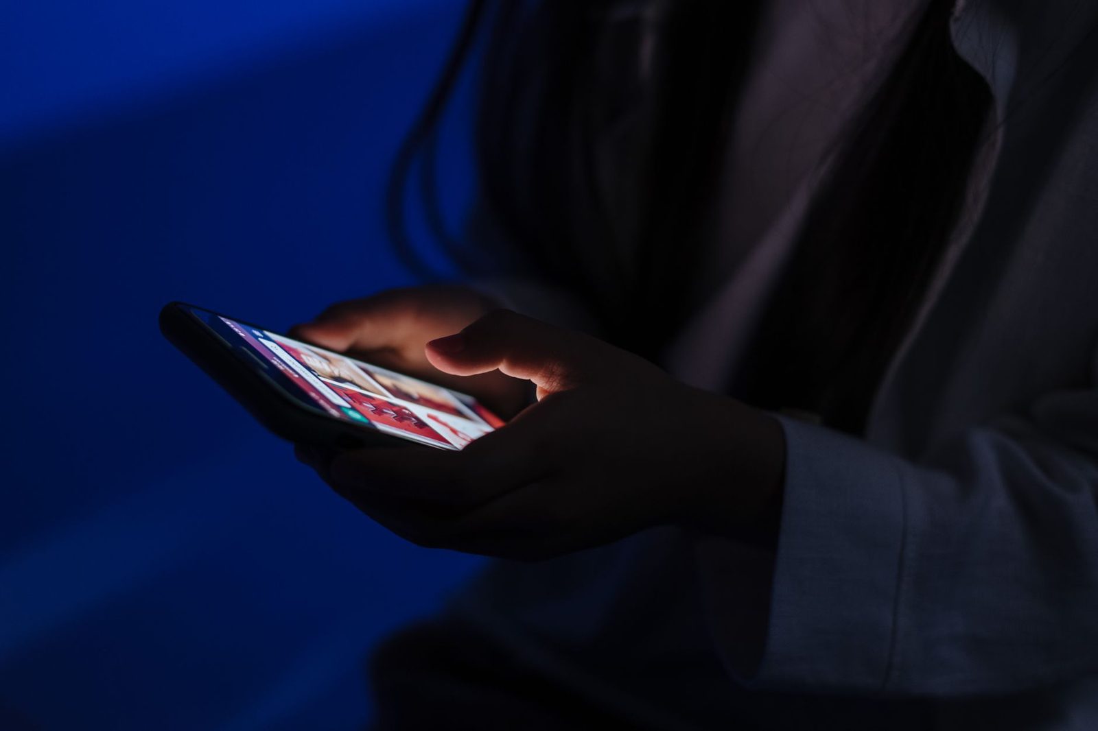 Mains d'une jeune femme tenant un smartphone allumé dans une pièce sombre à la lumière bleue