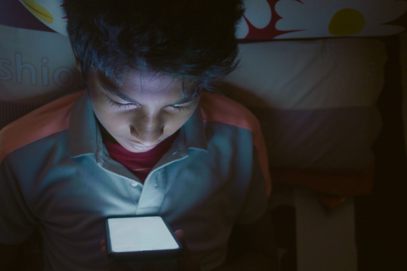 Jeune garçon dans une pièce sombre, le visage éclairé par l'écran de son smartphone tenu à deux mains