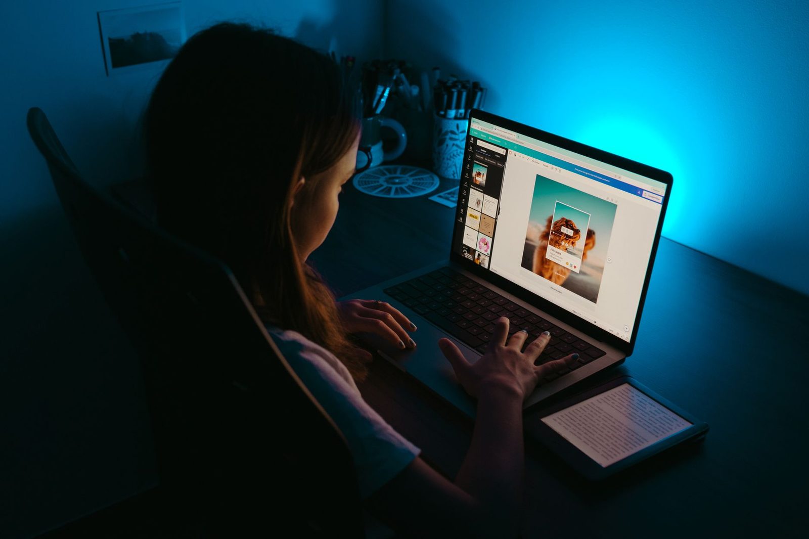 Jeune femme devant un ordinateur portable allumé dans une pièce sombre éclairée en bleu