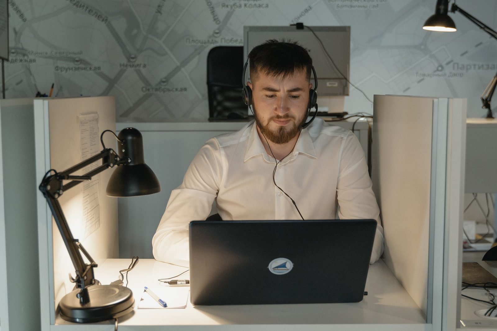 Homme avec un casque-micro assis devant un ordinateur portable dans un bureau éclairé par une lampe