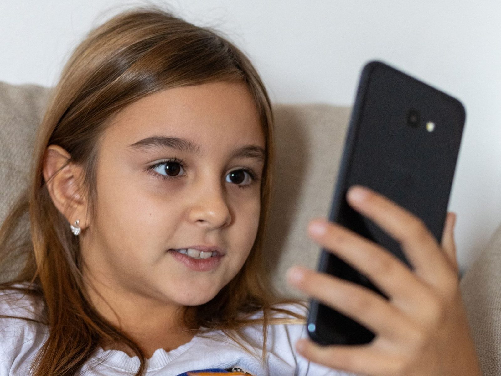 Jeune fille assise sur un canapé regardant l'écran d'un smartphone qu'elle tient à la main