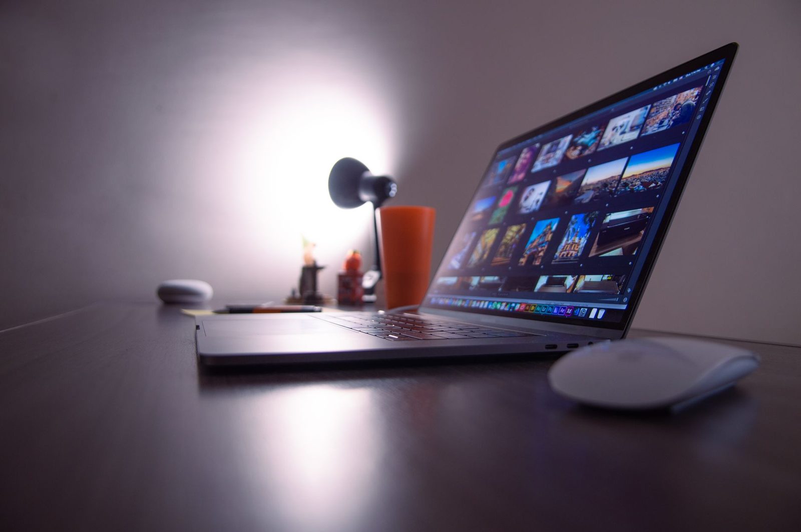 Ordinateur portable ouvert affichant une galerie de photos sur un bureau sombre, avec souris et lampe allumée