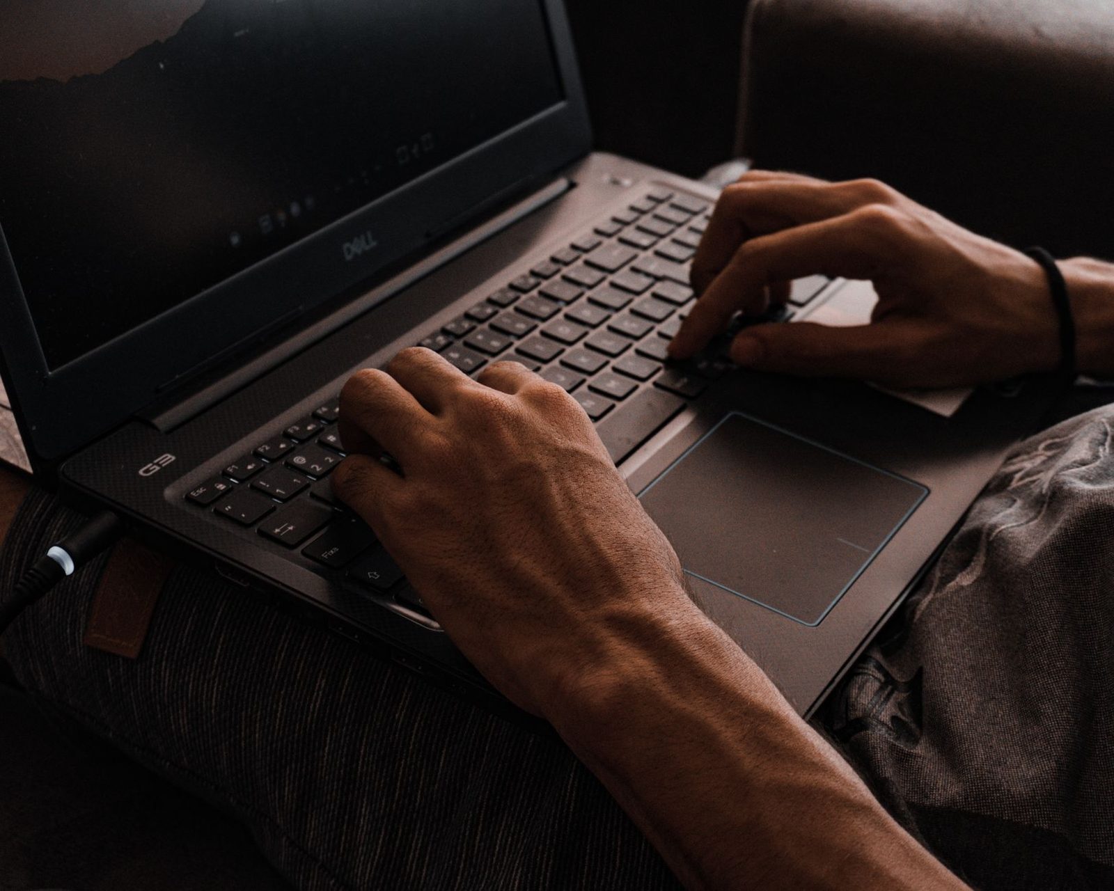 لقطة قريبة ليدَي رجل يكتب على لوحة مفاتيح حاسوب محمول موضوع على ركبتيه