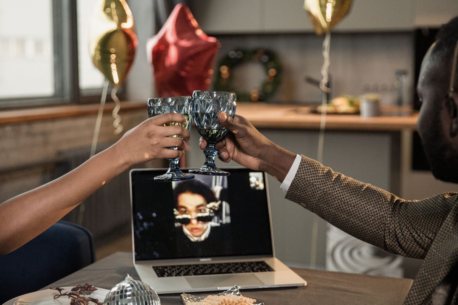 Deux personnes trinquent avec des verres au-dessus d'un ordinateur portable affichant un appel vidéo