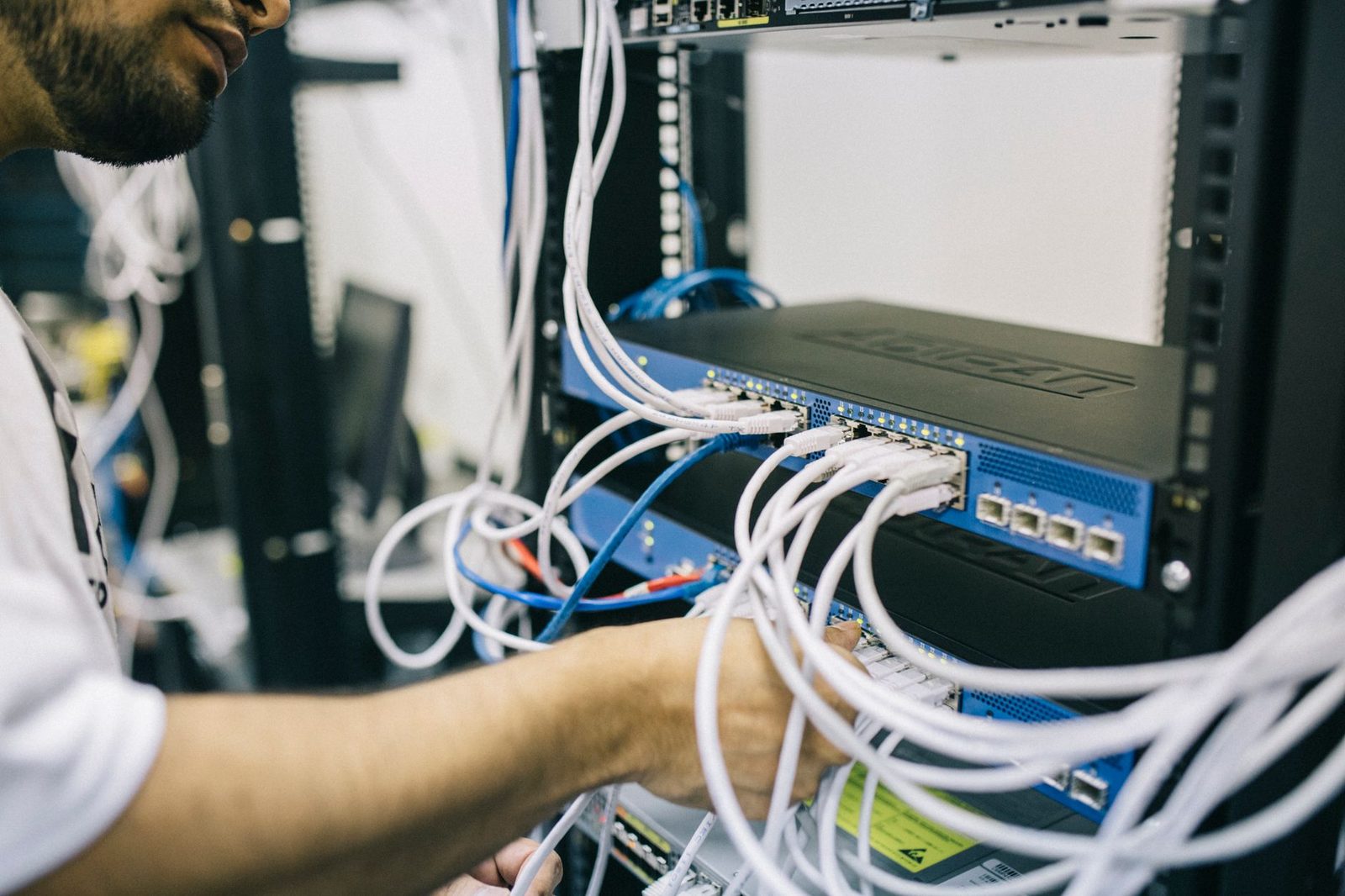 Technicien branchant des câbles Ethernet blancs sur un switch réseau bleu dans une baie de serveurs