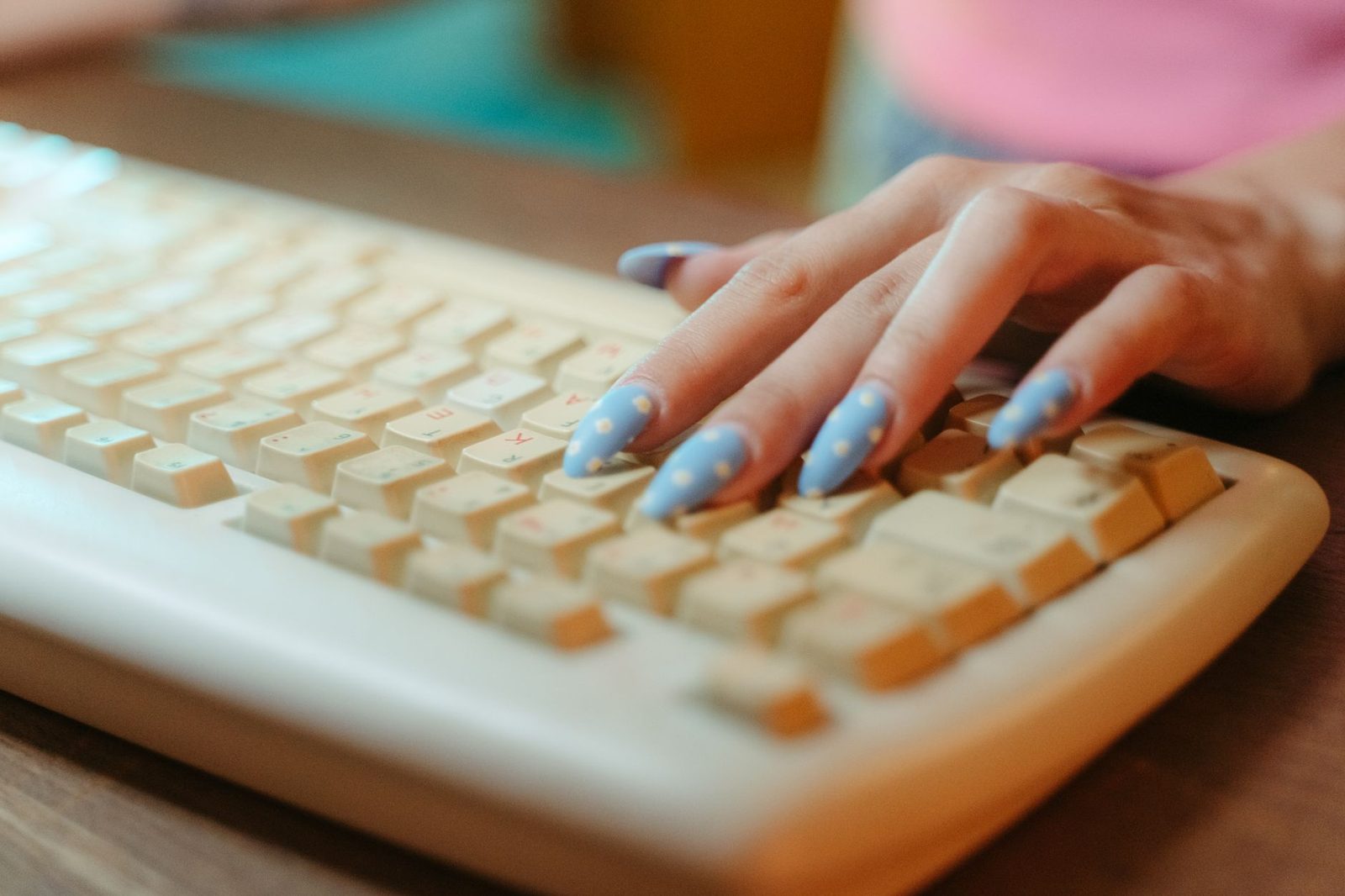 Main féminine aux ongles bleus tapant sur un clavier d'ordinateur blanc posé sur un bureau en bois