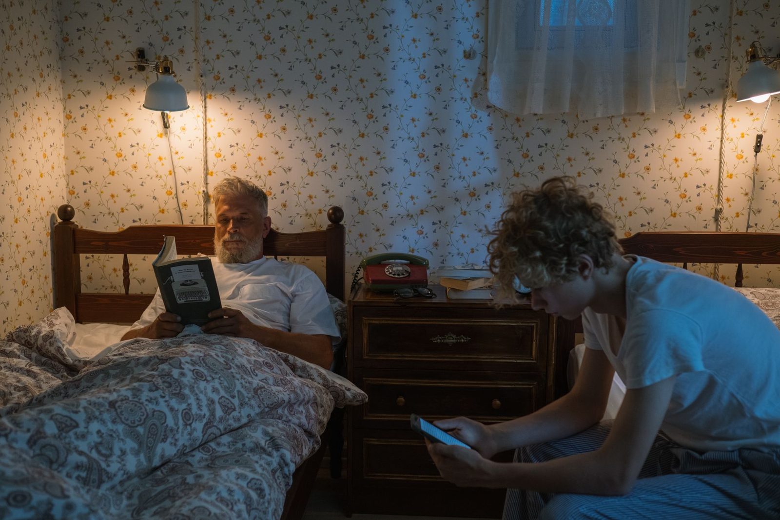 Adolescent sur un smartphone dans une chambre, un homme âgé lisant un livre au lit à côté