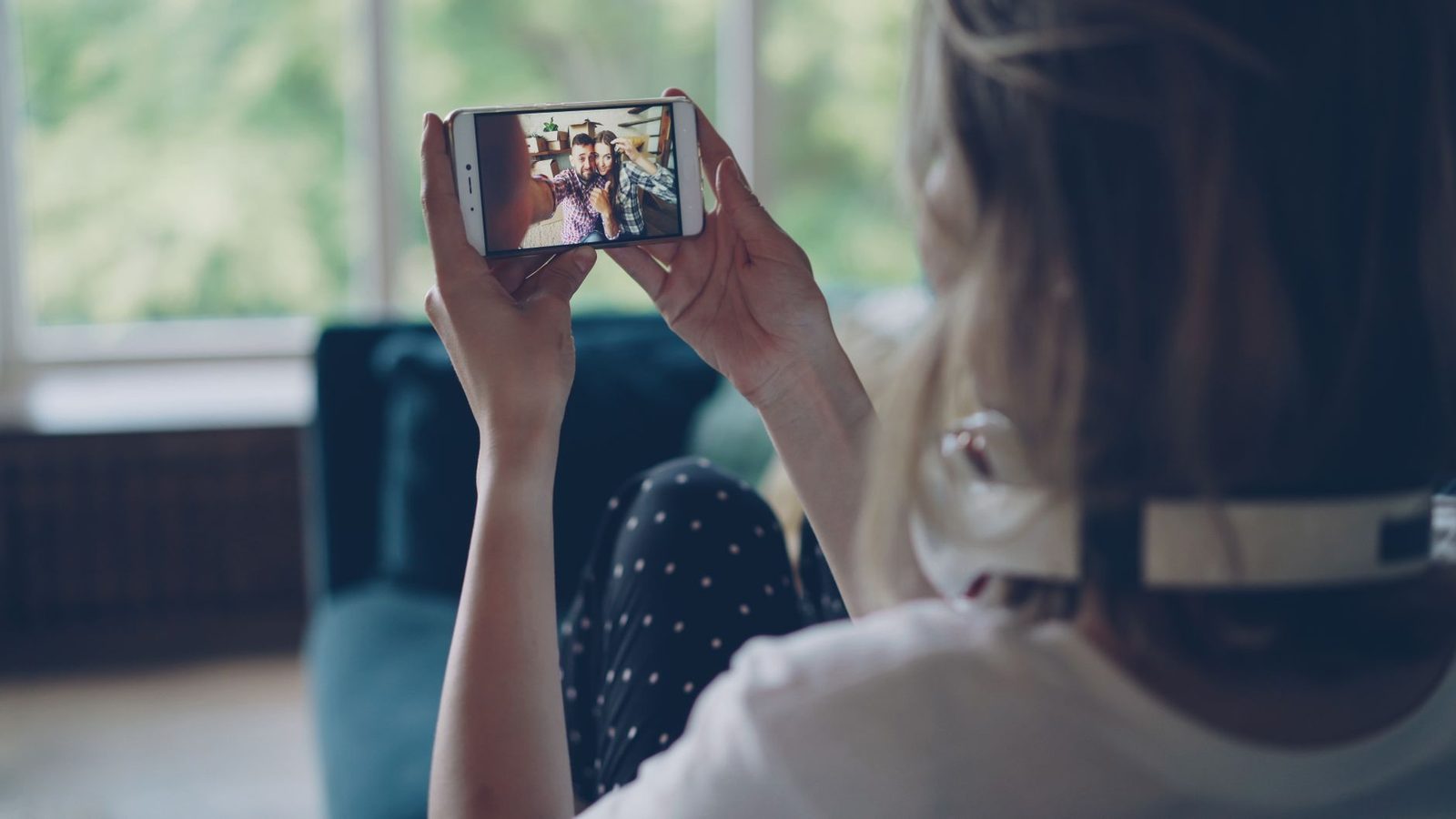 Une personne tenant un smartphone affichant un appel vidéo avec deux hommes.