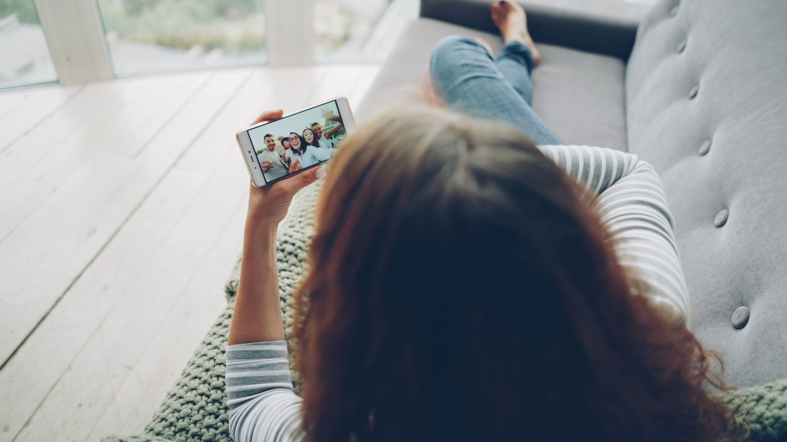 Une personne allongée sur un canapé regardant un appel vidéo sur son smartphone.