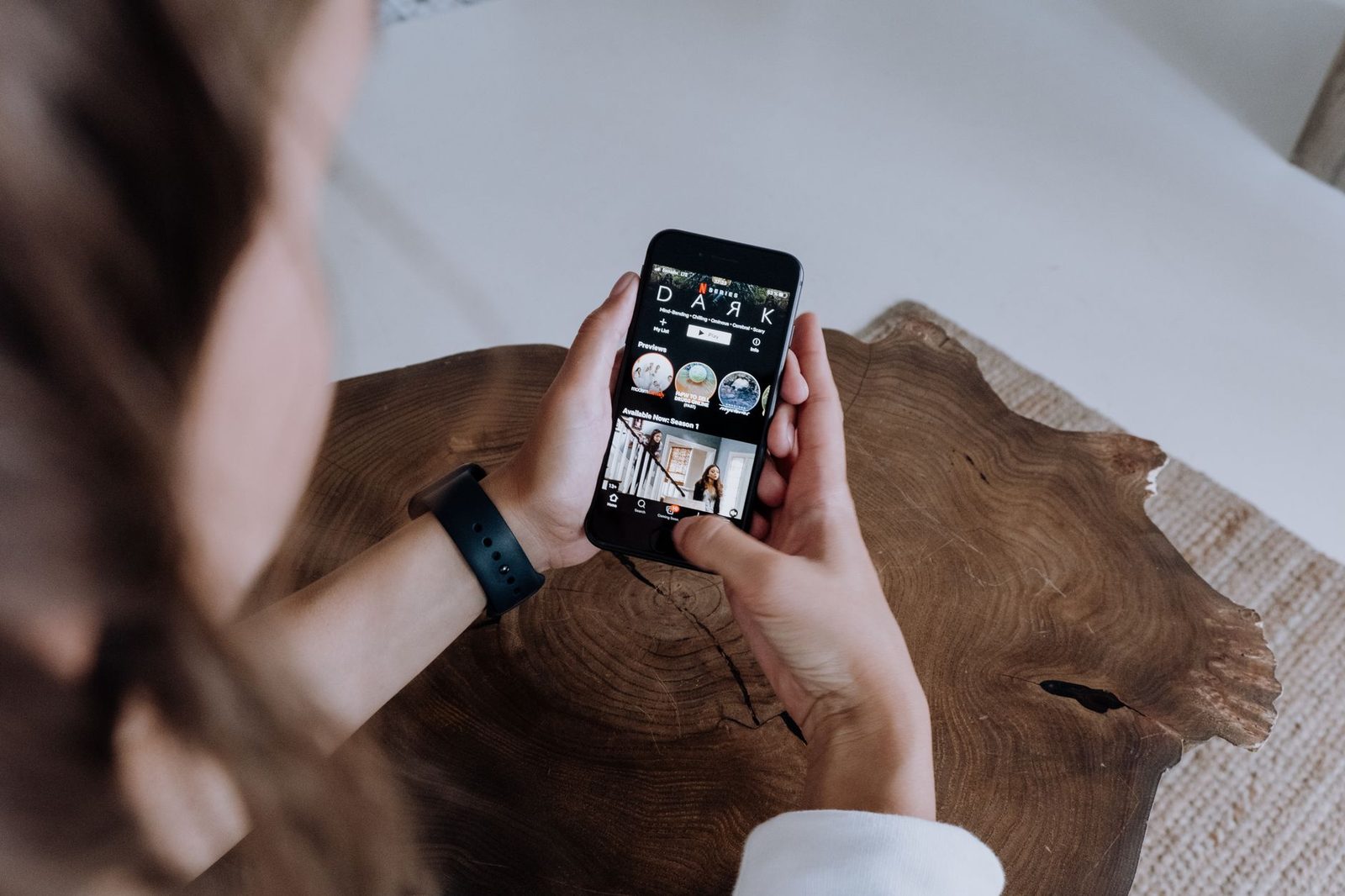Mujer sosteniendo un smartphone con una aplicación de streaming en pantalla sobre una mesa de madera