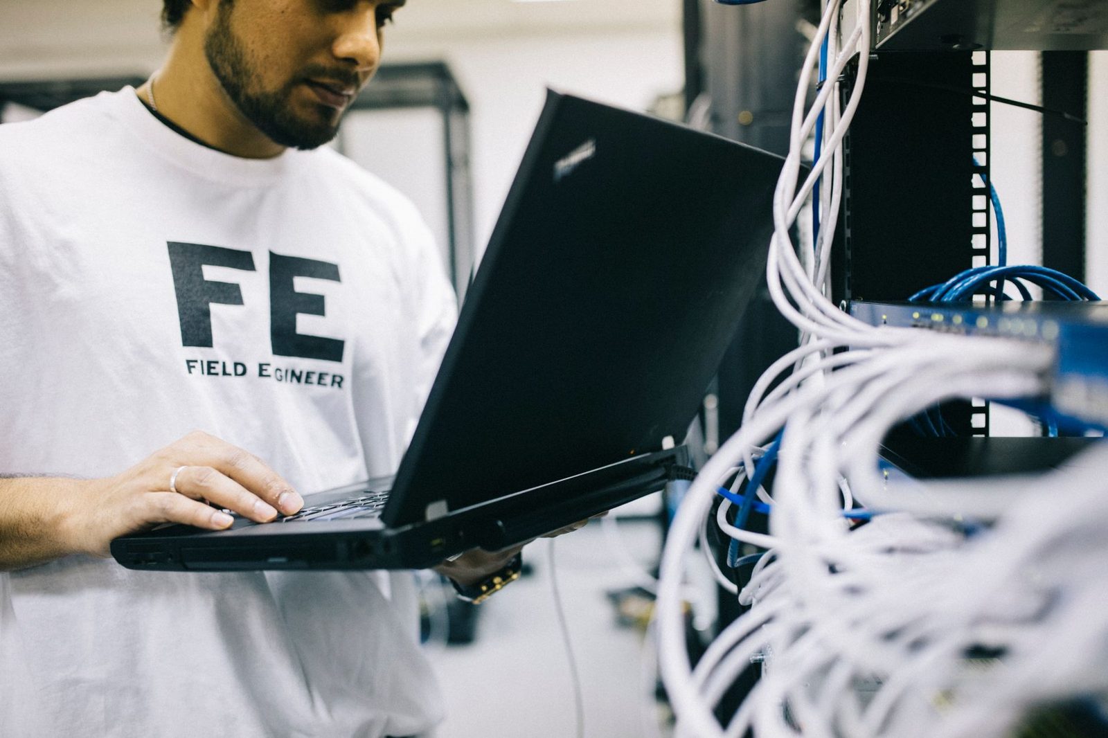 Técnico de redes con un ordenador portátil frente a un rack de servidores lleno de cables Ethernet
