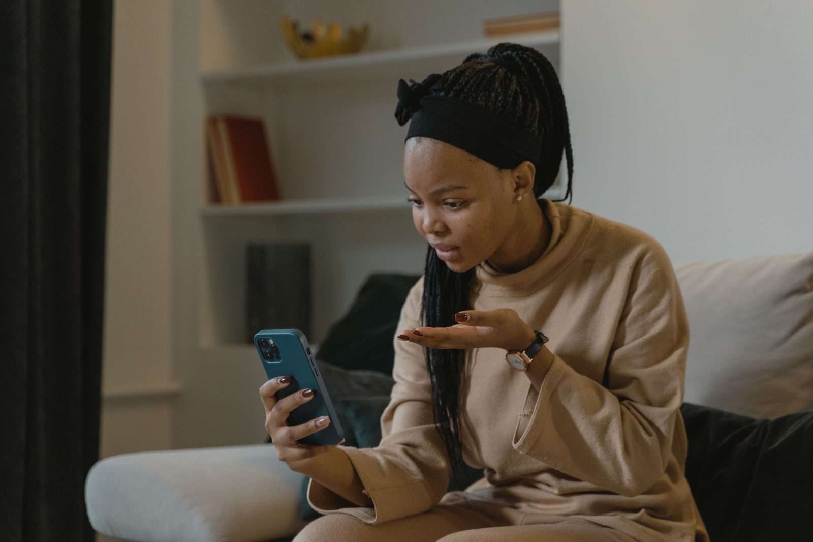 Jeune femme assise sur un canapé en pleine conversation vidéo sur son smartphone
