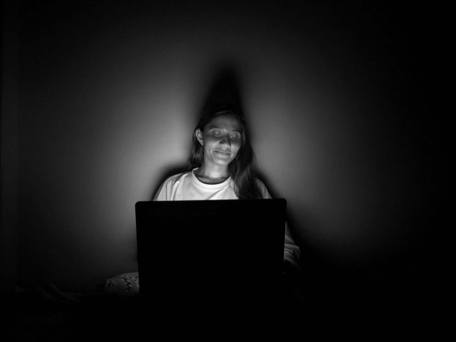 Photo en noir et blanc d'une jeune femme dans le noir, visage éclairé par l'écran de son ordinateur portable