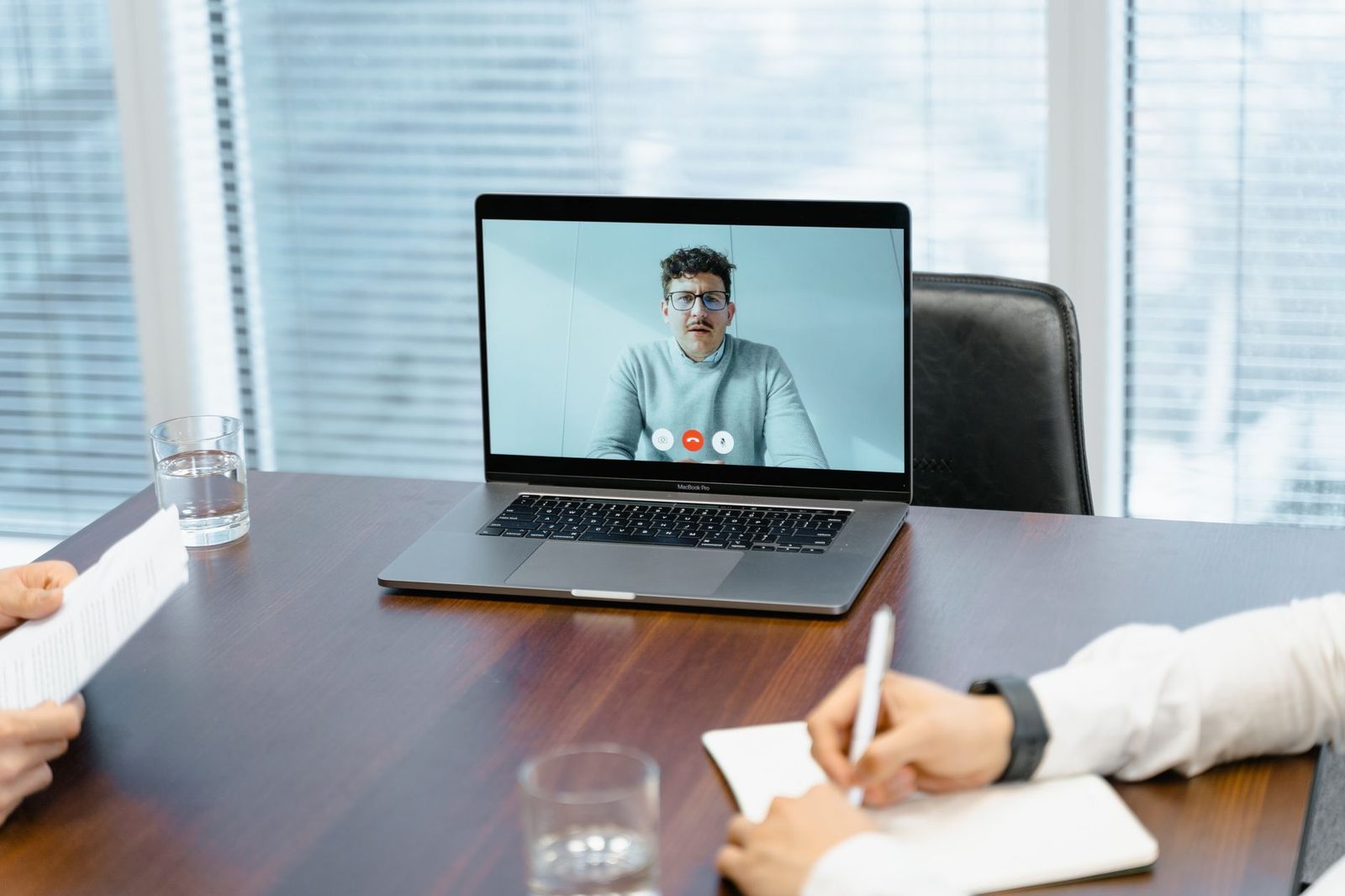 Appel vidéo sur un ordinateur portable posé sur une table de réunion, homme visible à l'écran